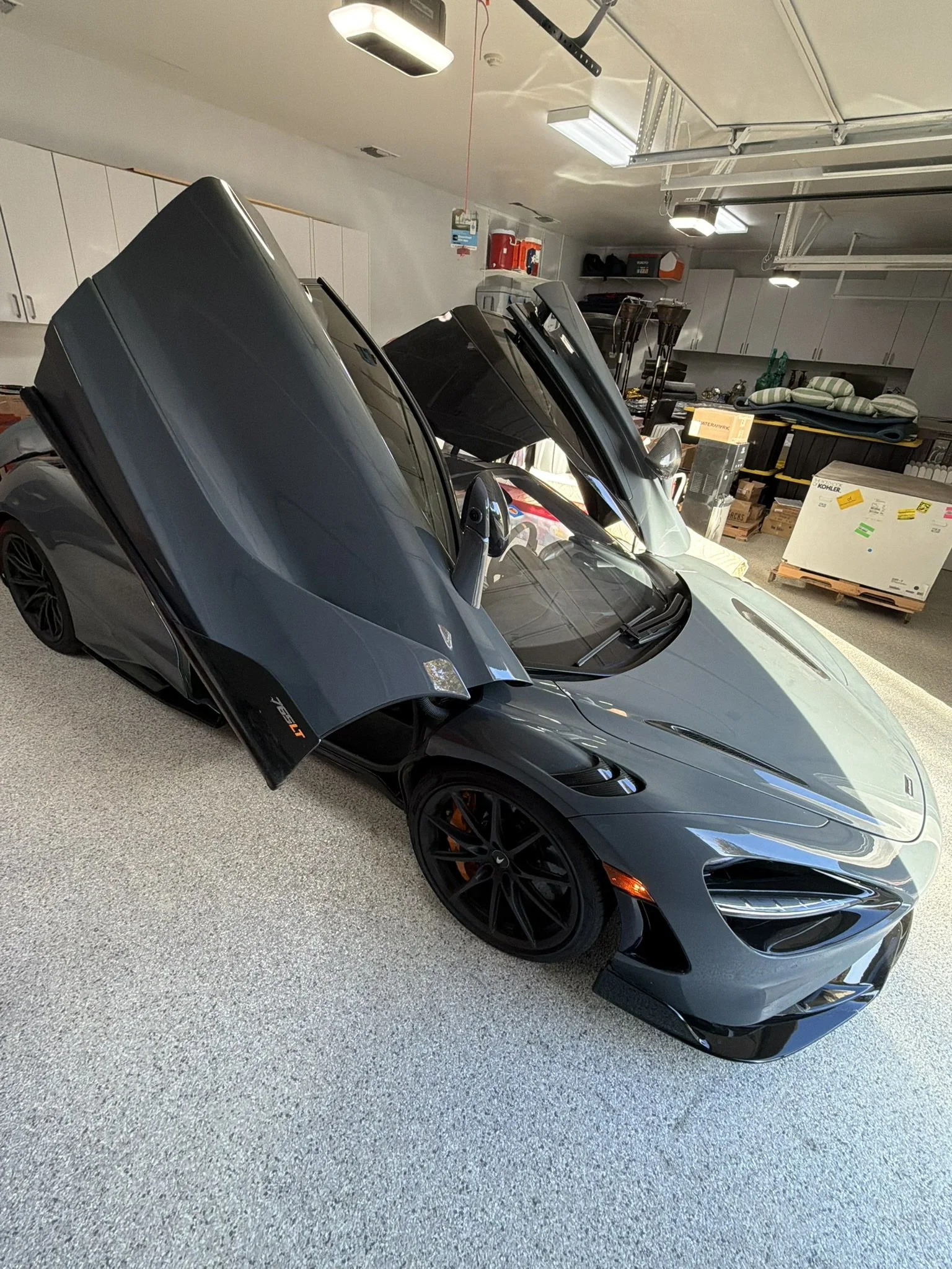 A gray sports car with its gullwing doors open inside a garage.