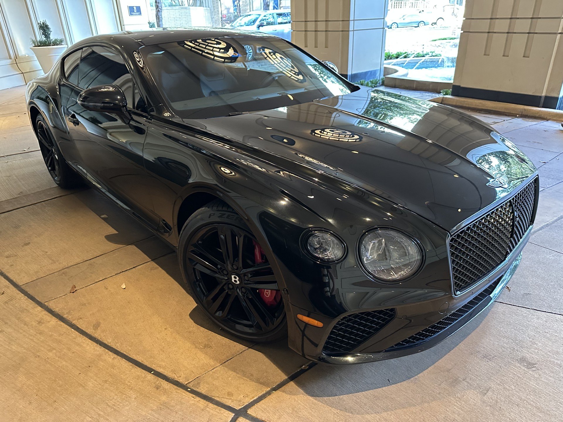 A black luxury sports car displayed indoors, featuring a sleek design, black wheels, and red brake calipers.