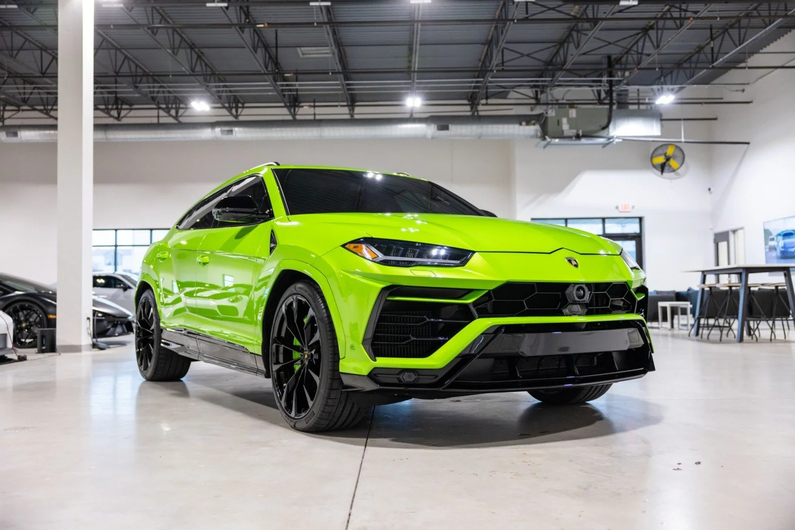 Bright green Lamborghini SUV inside a showroom with other cars and modern furniture.
