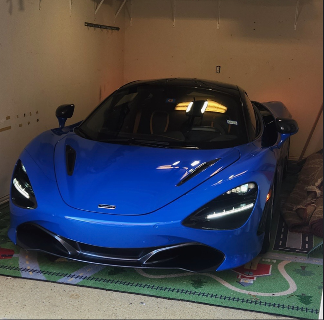 Blue sports car parked in a garage with a patterned rug underneath.