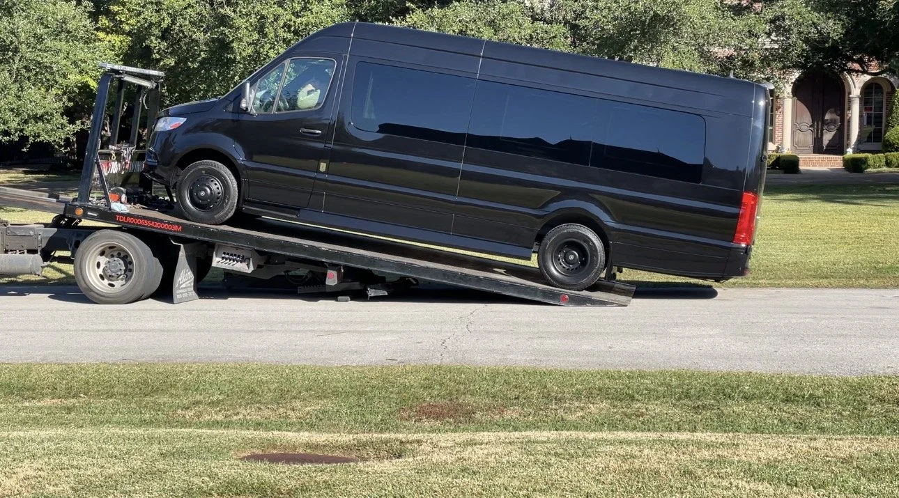 Black van loaded onto flatbed tow truck on a residential street.