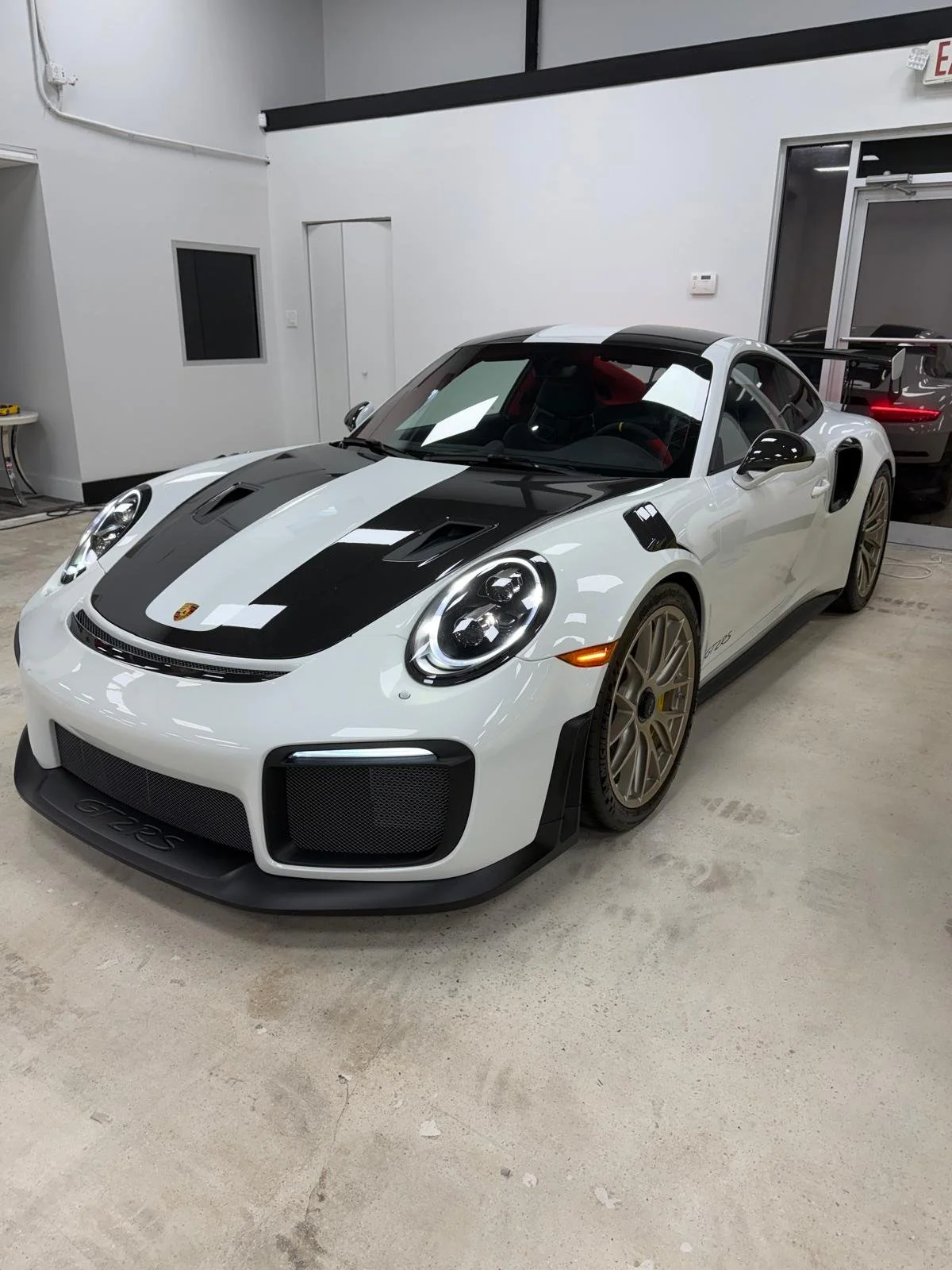 A white Porsche 911 GT2 RS sports car with black racing stripes parked indoors.