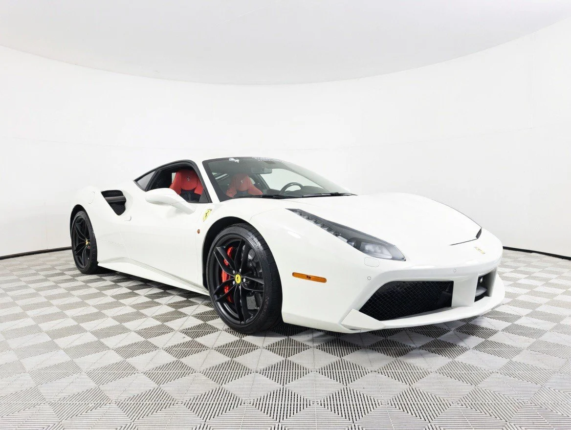 White Ferrari sports car with black wheels and red interior in a studio with white background.
