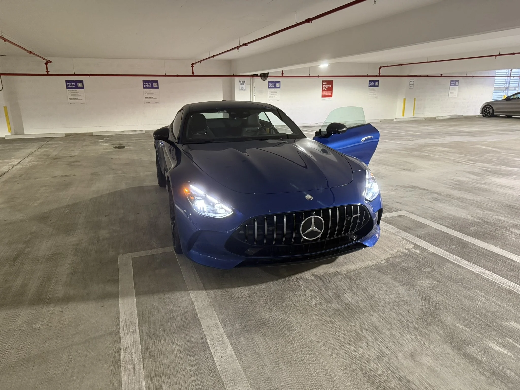 A blue Mercedes-Benz car parked in an underground parking garage with one door open.