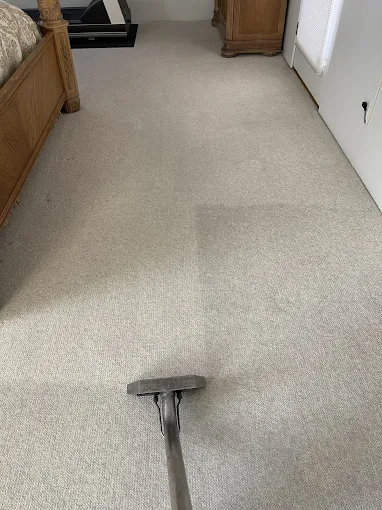 A carpet being steam cleaned in a bedroom with a wooden bed frame and a wooden dresser.