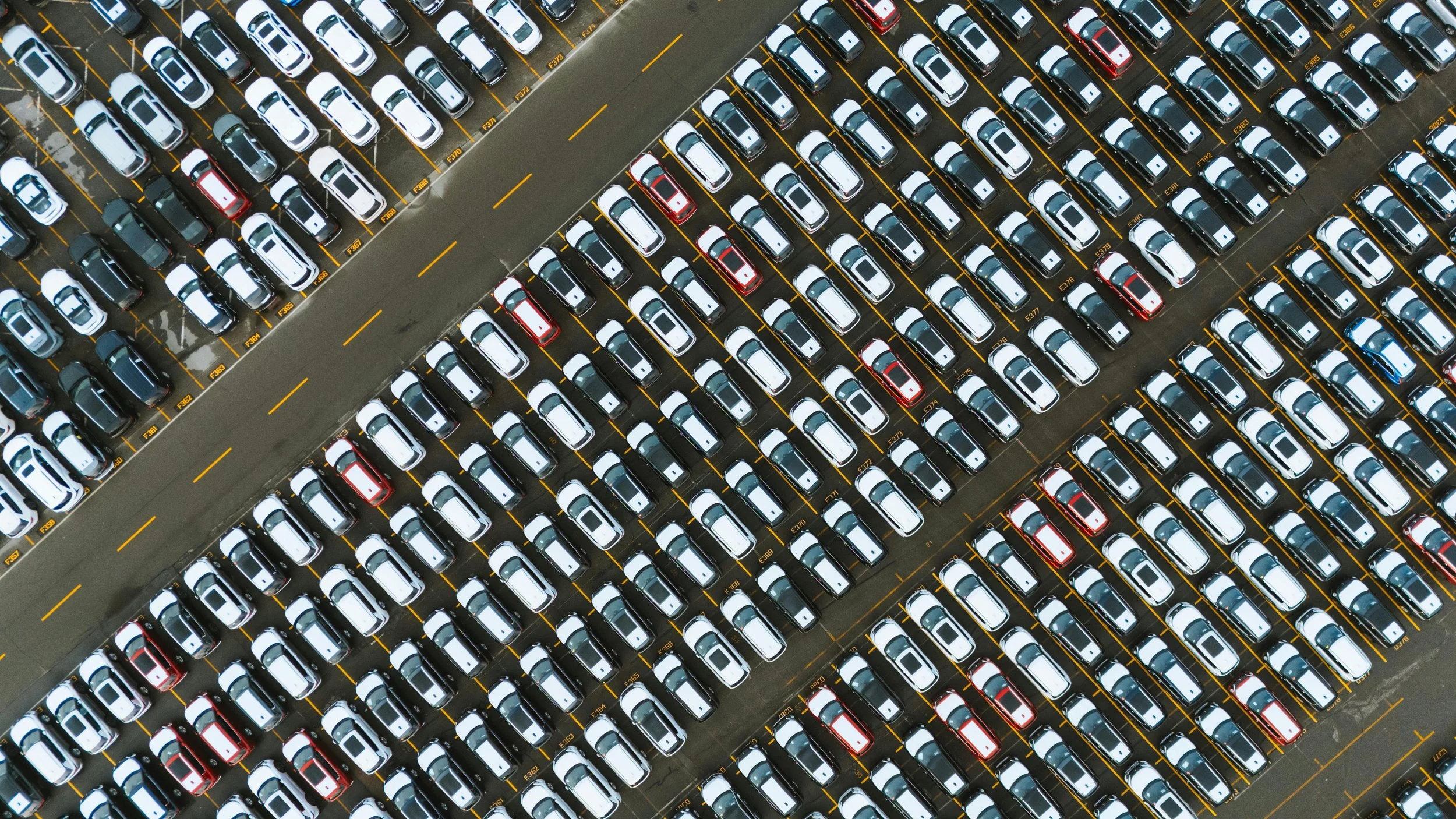 An aerial view of a parking lot filled with cars arranged in rows, with a section of empty parking spots and a lane separating two sections.