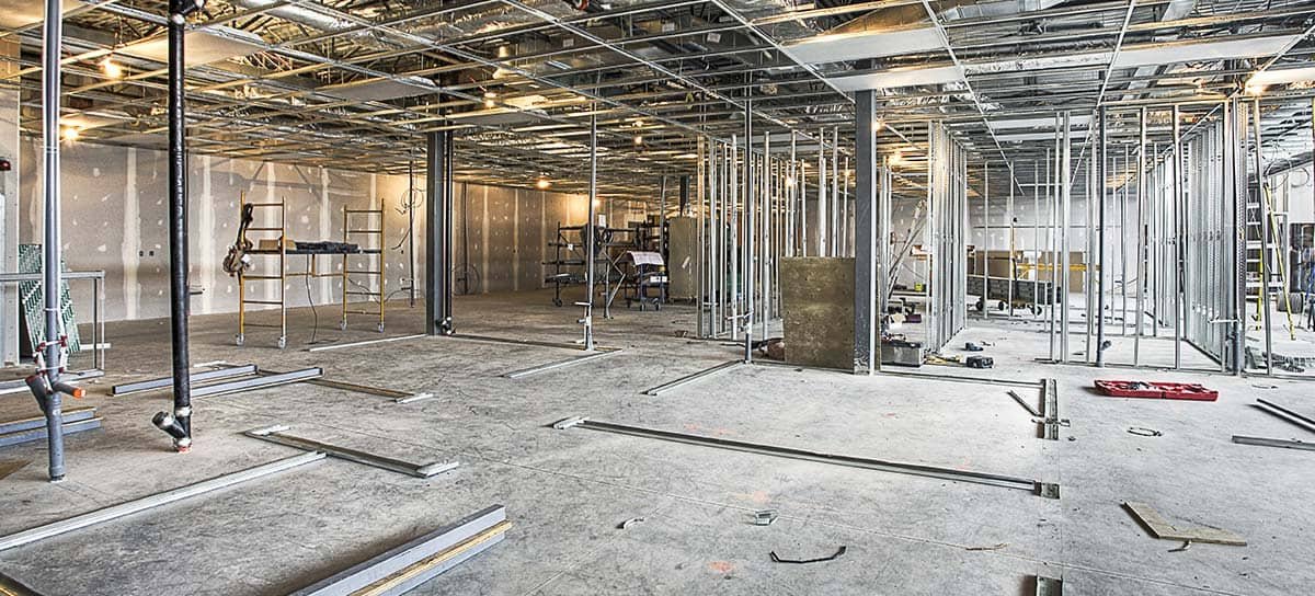 Interior of a building under construction with metal framing, scaffolding, and construction tools scattered on the floor.