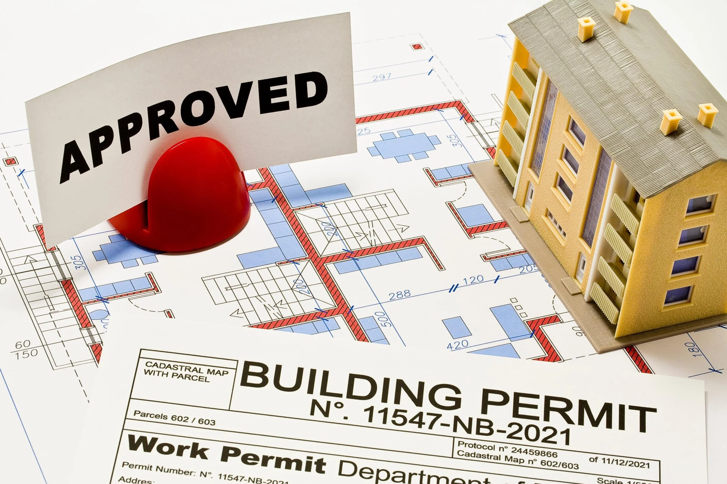 A house model, a permit form, and an 'Approved' sign on architectural blueprints, indicating building approval.