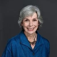 Portrait of an older woman with gray hair smiling, wearing a blue blouse and a black necklace.