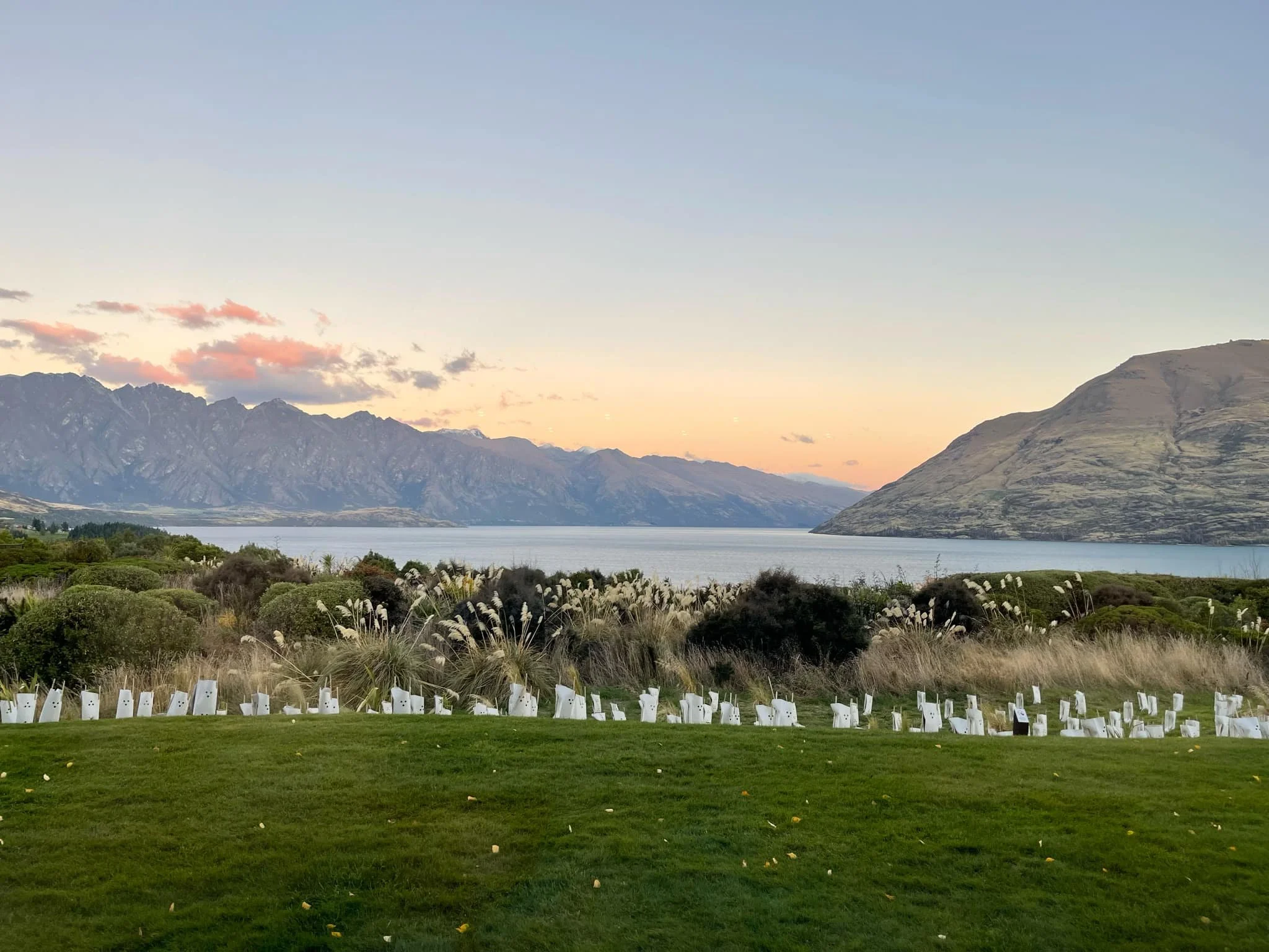 Scenic view of a lake with mountains in the background at sunset, with a well-maintained grassy area