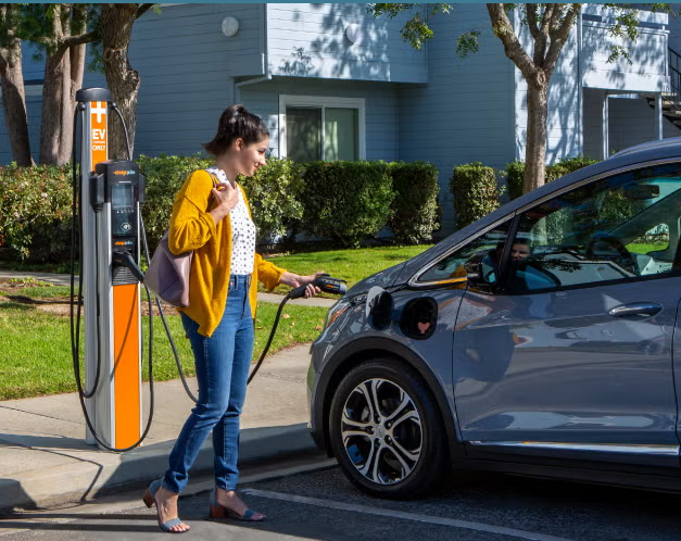 Woman in yellow jacket charging electric car at charging station on city street