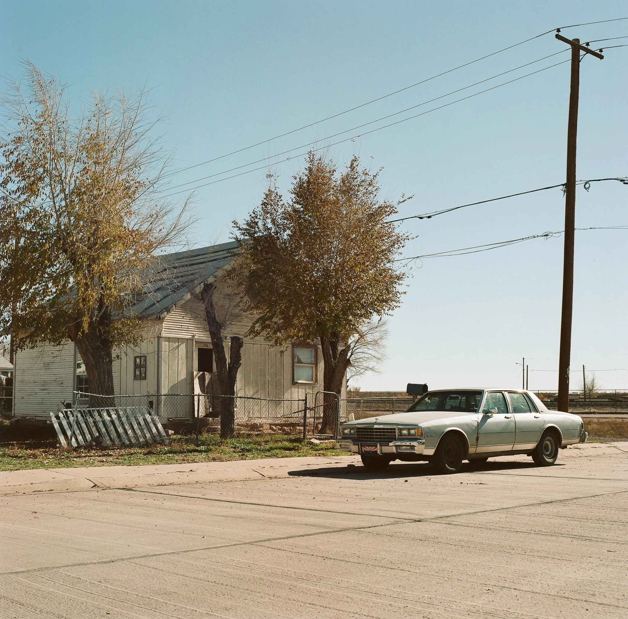 An old caprice out front of a small old house in the desert