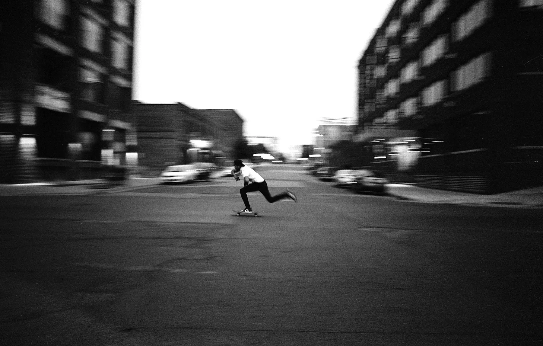 Person skateboarding through an intersection downtown at dusk