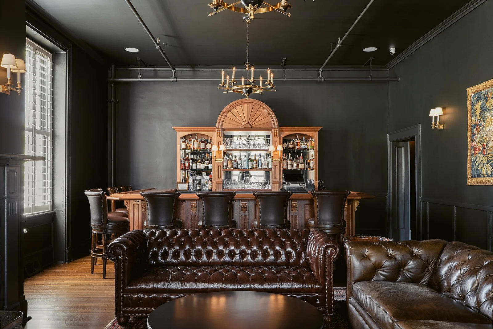 Carlisle's Restaurant Lounge in Hotel Everett | Boutique Hotel in Winnsboro, SC, historic hotel | Elegant bar area with dark walls, wooden bar counter, leather bar stools, and a variety of liquor bottles behind the bar.