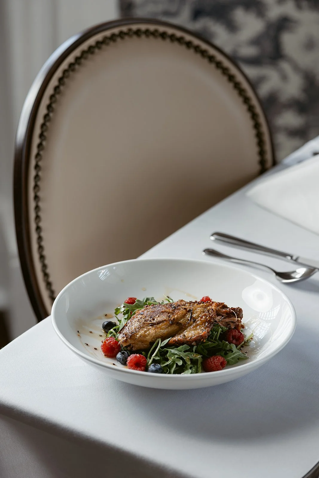 A plate of Roasted Chicken with sage butter, garlic mashed potatoes, squash casserole on a white tablecloth, with silverware nearby, in a restaurant setting.