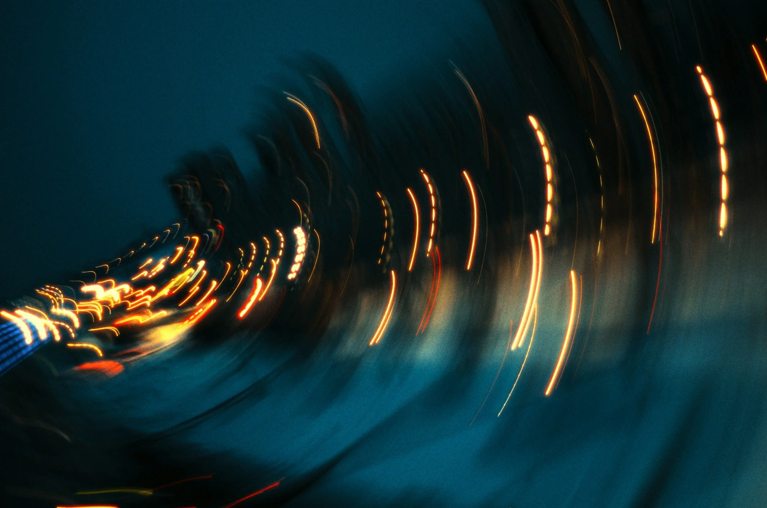 Blurred lights on a road at night, creating streaks of yellow, orange, red, and white against a dark blue sky.