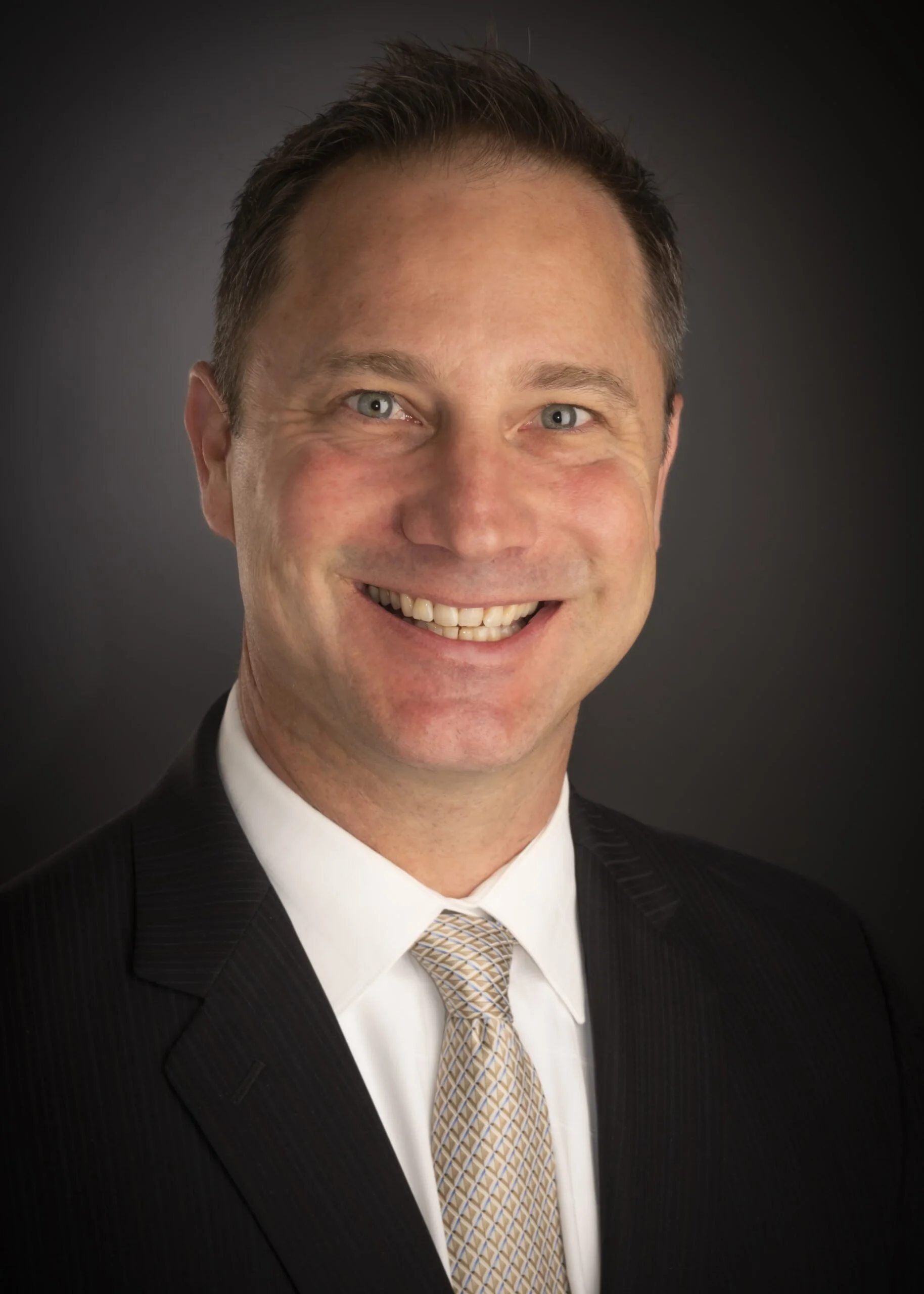 A smiling man in a black suit, white shirt, and a beige patterned tie against a dark background. Nathan Whitenton is the author of The Tao of Mission Assurance | Technical Risk Leadership for Aerospace and Critical Mission Systems.