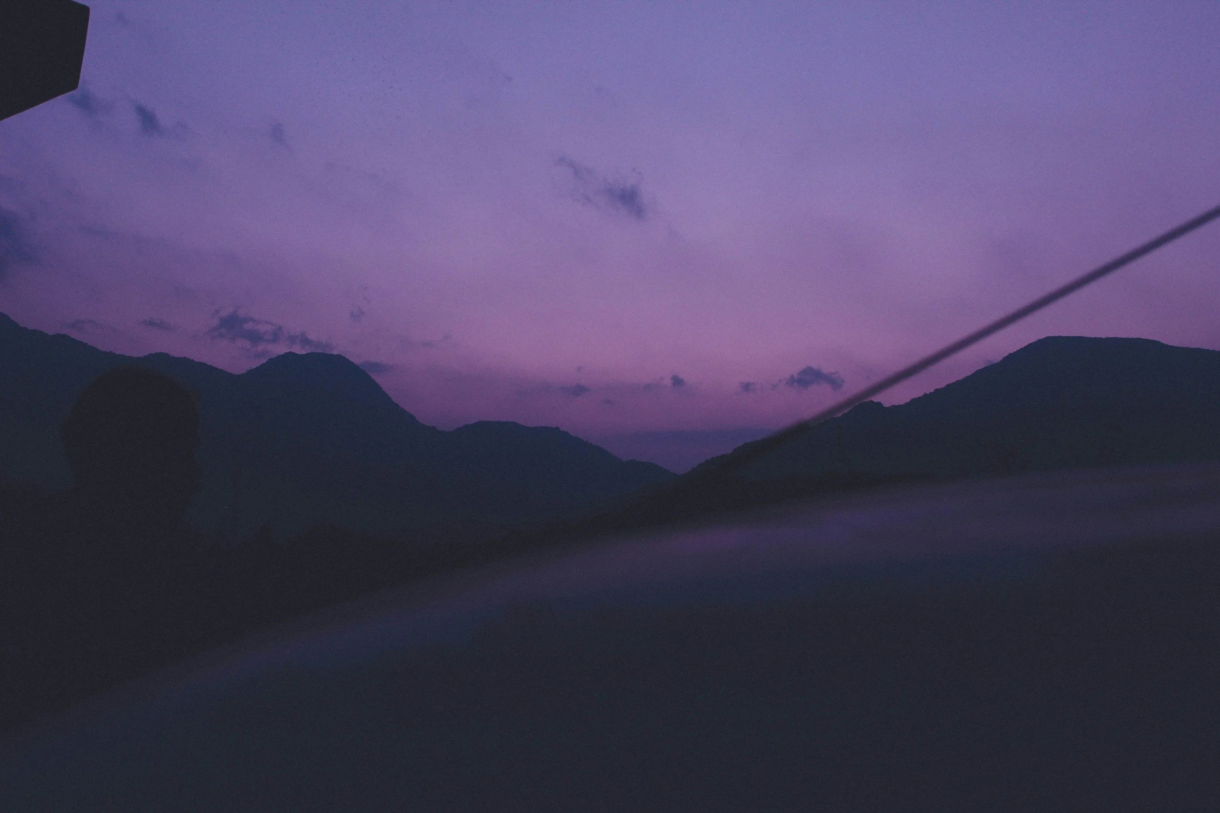 A landscape view of mountains silhouetted against a purple twilight sky with scattered clouds.