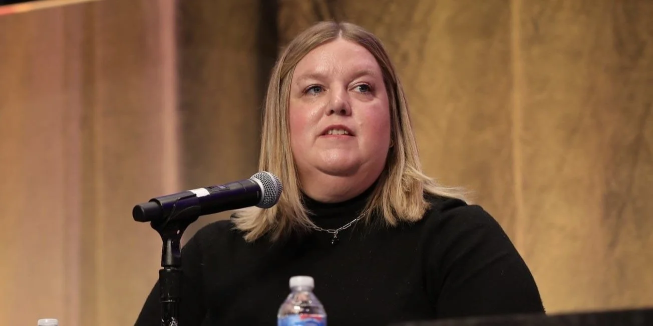 Jenn Patrice Schultz, a woman with blonde hair speaking into a microphone on a panel at an event.