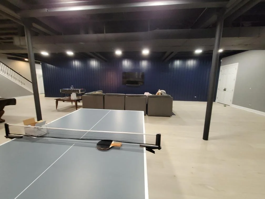 Indoor game room with a ping pong table in the foreground and a seating area with a couch and television in the background.