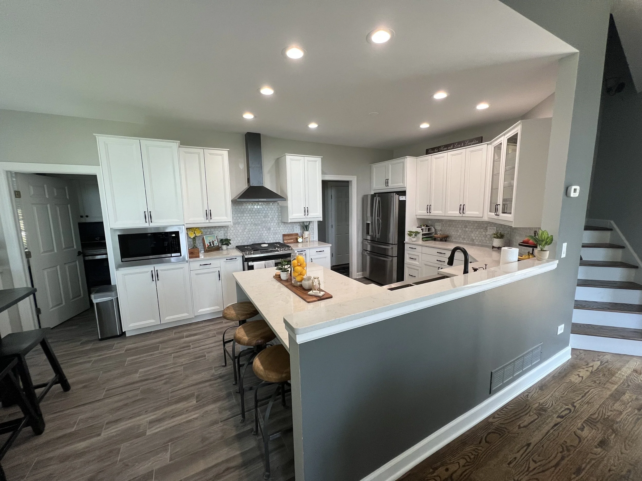 Modern kitchen with white cabinetry, stainless steel appliances, a central island with bar stools, and wooden flooring.