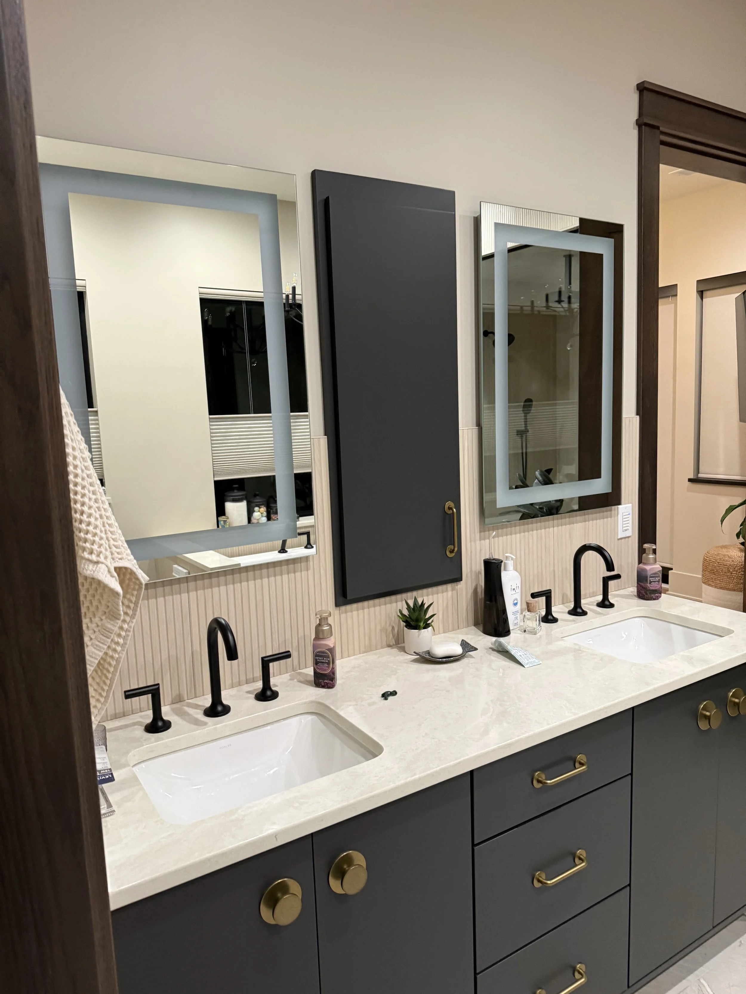 Double bathroom vanity with two black faucets, dark blue cabinets with gold hardware, and large mirrors in a modern bathroom.