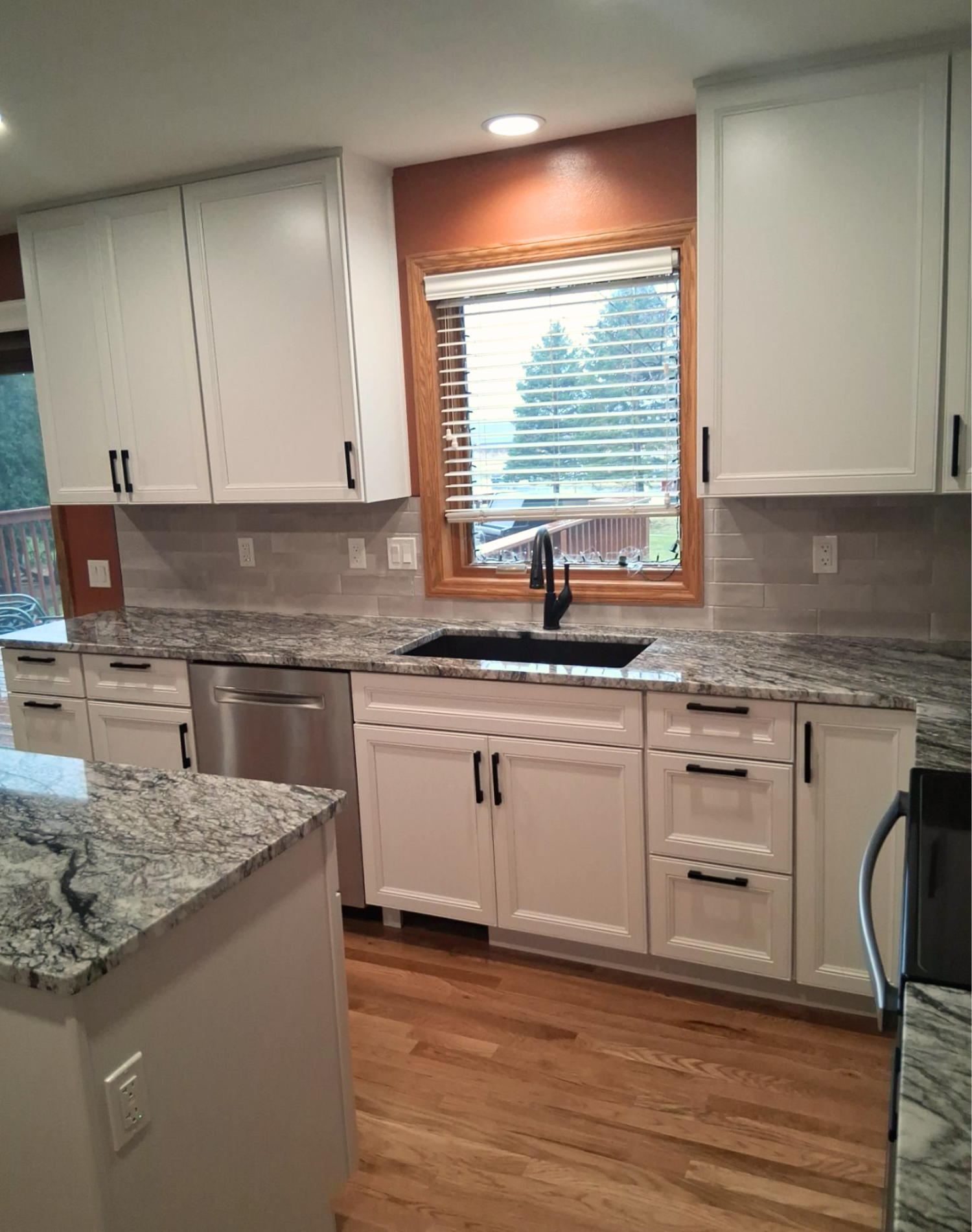 Modern kitchen with white cabinets, granite countertops, a black sink, a window with wooden trim, and hardwood flooring.