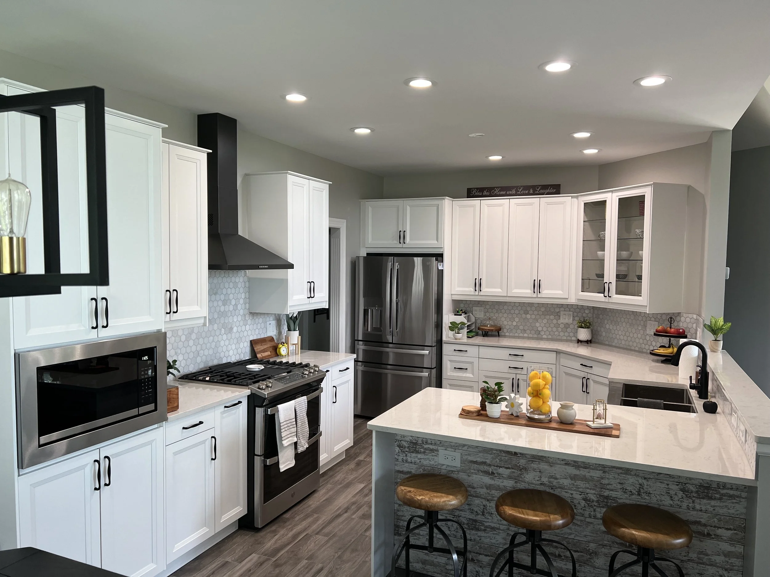 Modern kitchen with white cabinets, stainless steel appliances, a central island with bar stools, and decorative plants and lemons on the counter.