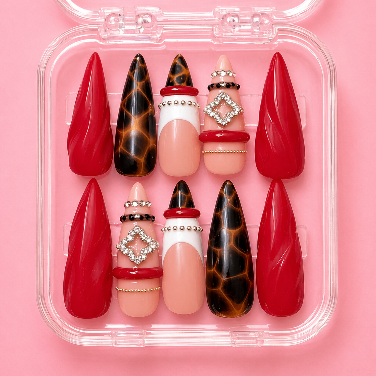 A plastic case filled with decorative false nails in red, tortoise shell, pink with rhinestone and bead embellishments, on a pink background.