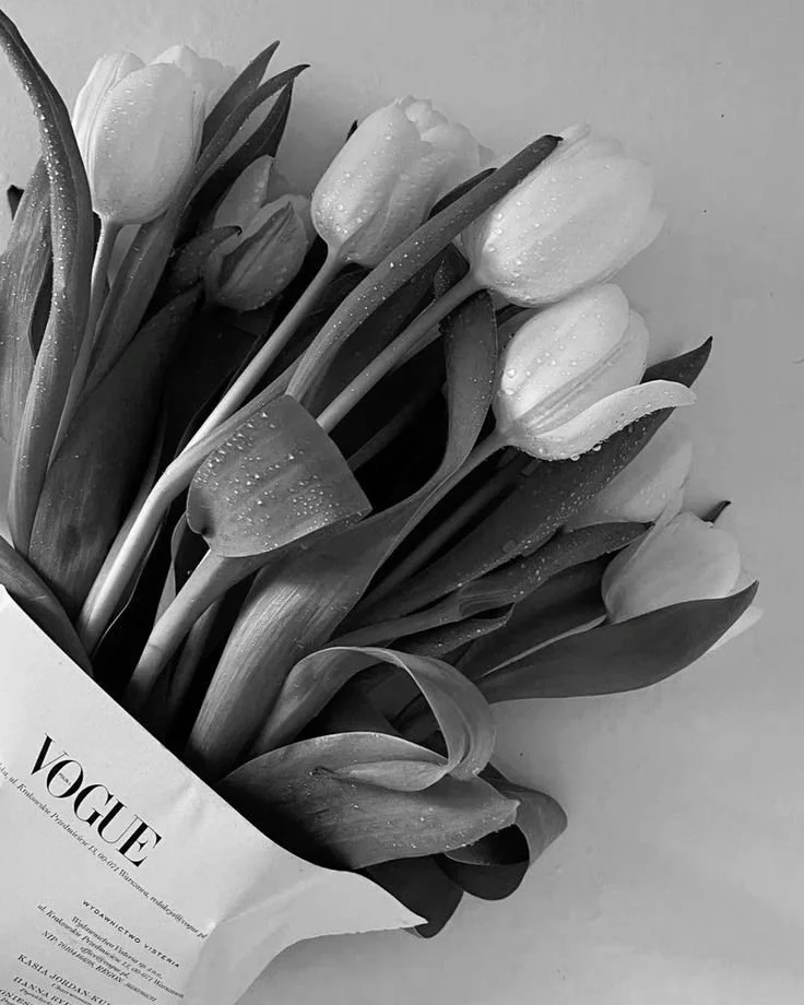 A bouquet of tulips wrapped in Vogue paper with water droplets visible on the petals and leaves.