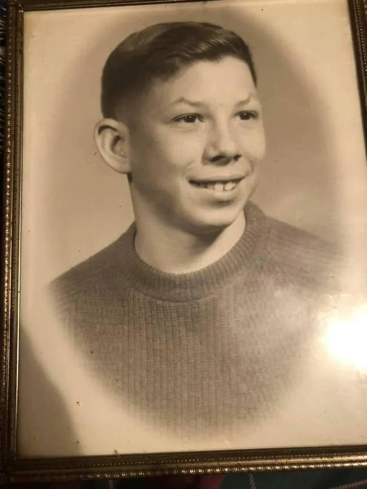 A sepia-toned school portrait of a teenage boy in a crew-neck sweater, framed in a decorative frame.