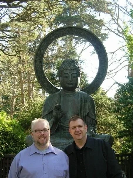 Two men standing together in front of a bronze Buddha statue at the Japanese Tea Garden in San Francisco.