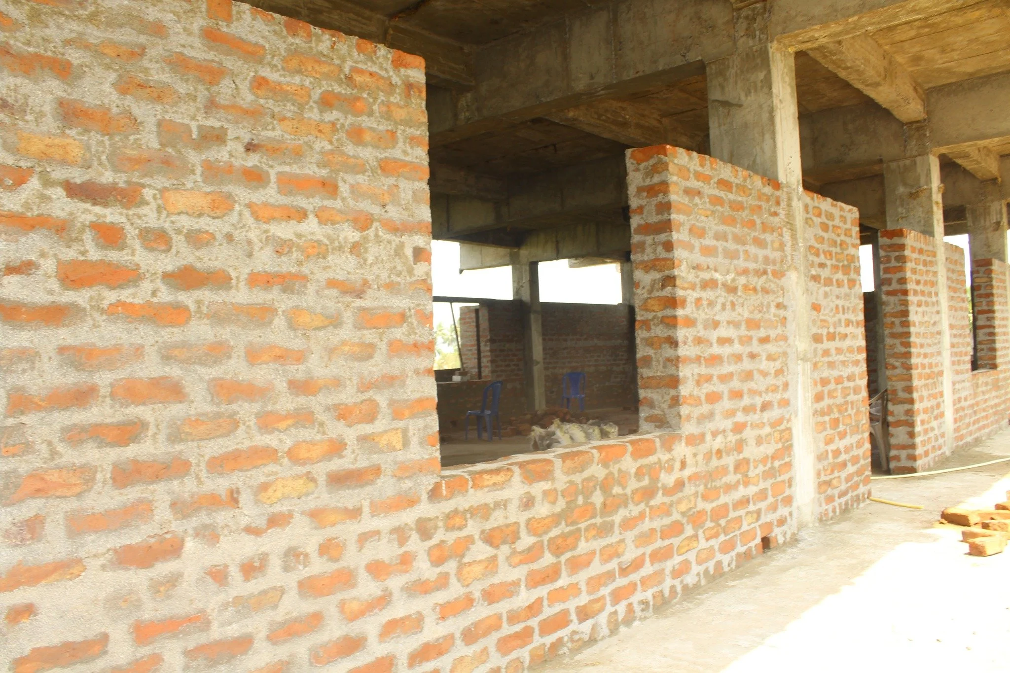Brick wall under construction with open window spaces and visible concrete structure in the background.
