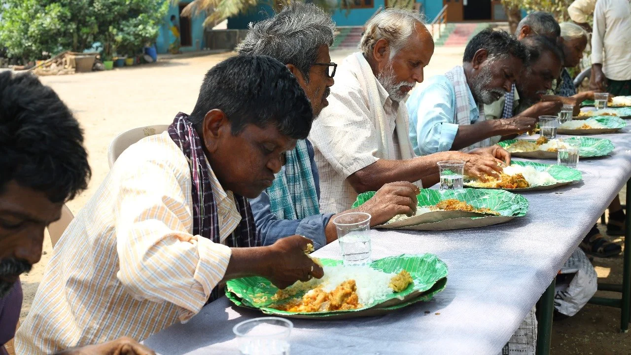 People eating traditional Indian meal outdoors at a long table.