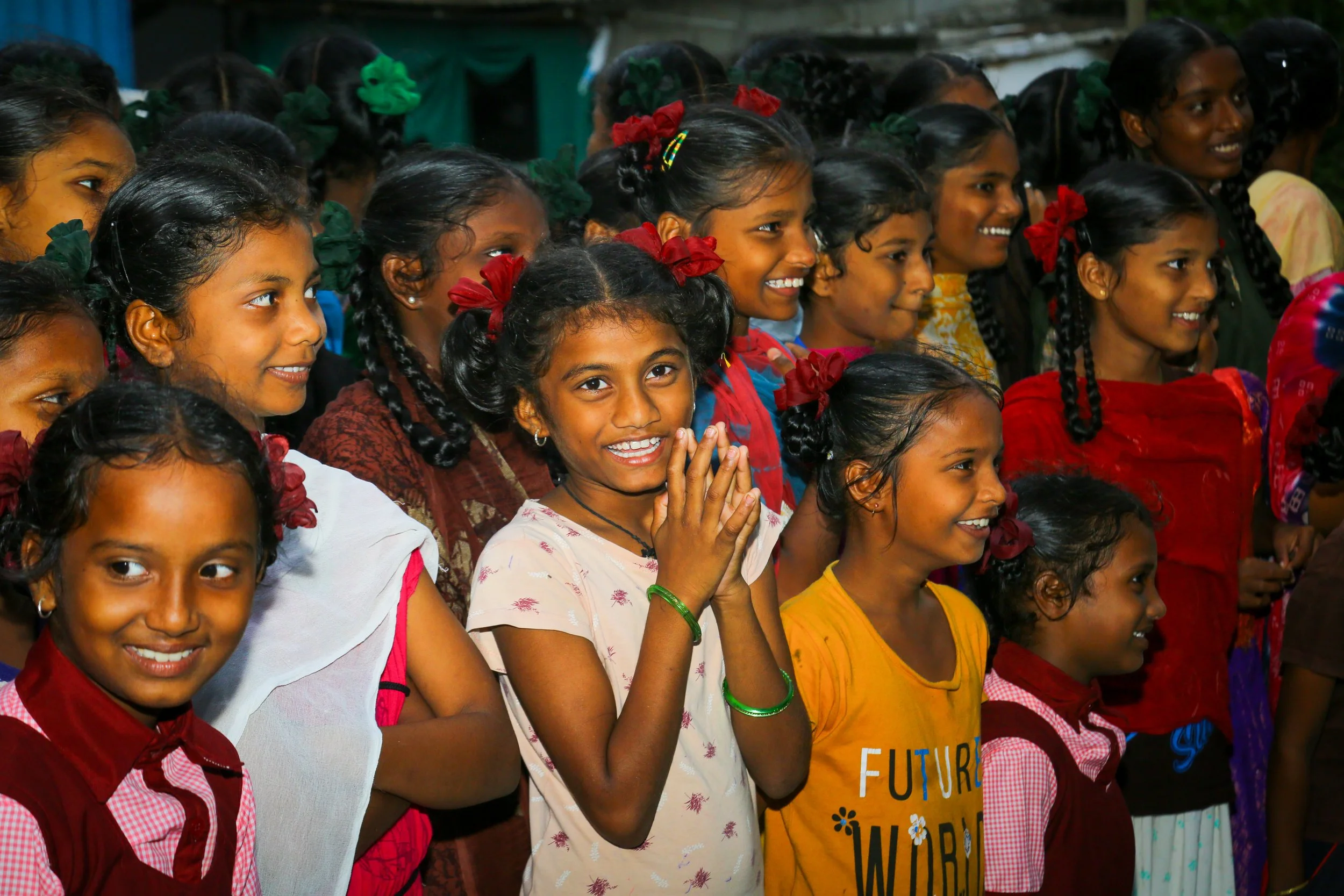 Group of smiling young girls with braided hair and colorful clothing, gathered together.