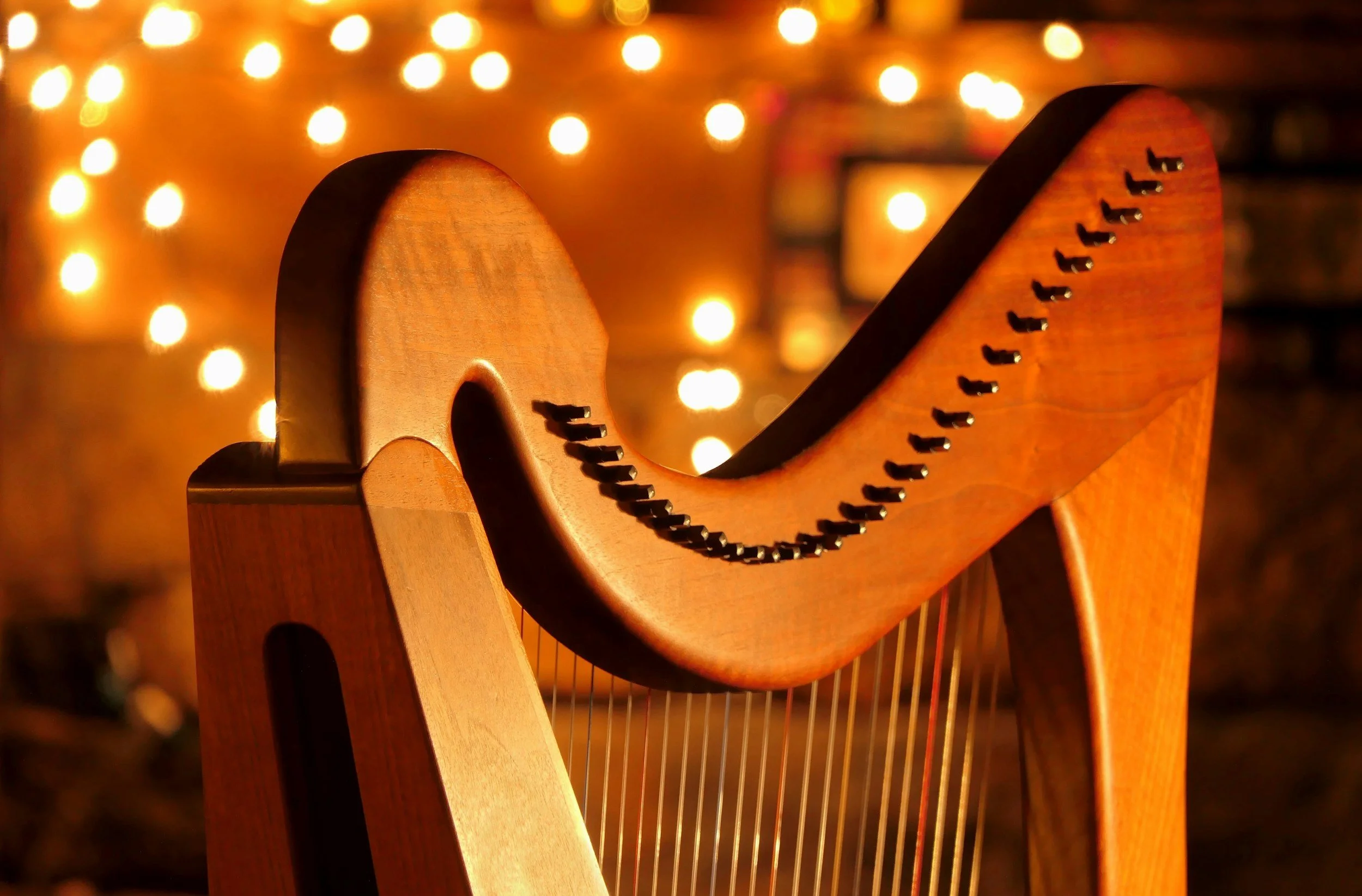 Close-up of a wooden harp with illuminated string pins, background of warm glowing string lights