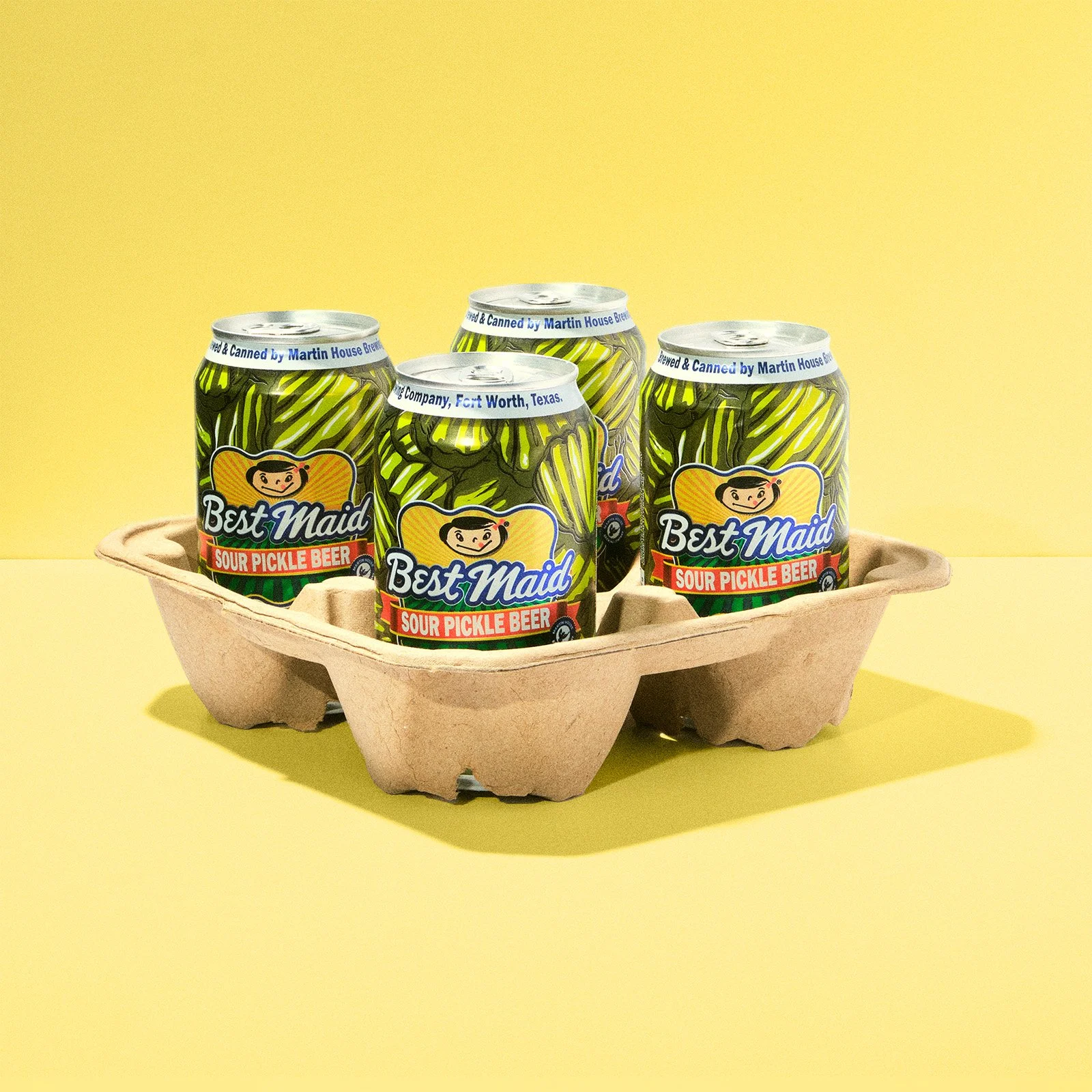 Four cans of Best Maid Sour Pickle Beer in a cardboard tray on a yellow background.