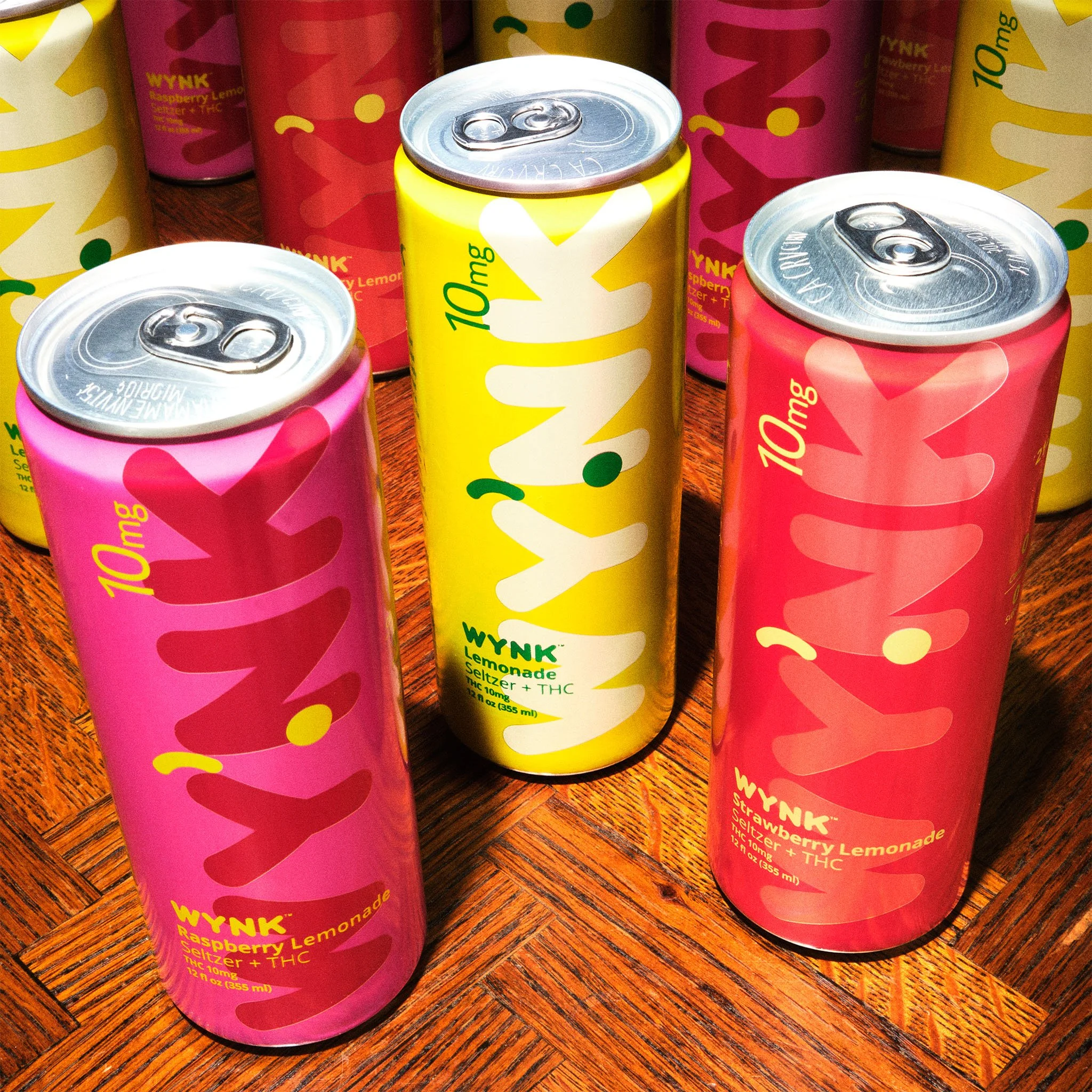 Cans of WYNK Lemonade, featuring Raspberry Lemonade, Strawberry Lemonade, and Lemonade flavors, placed on a wooden surface.