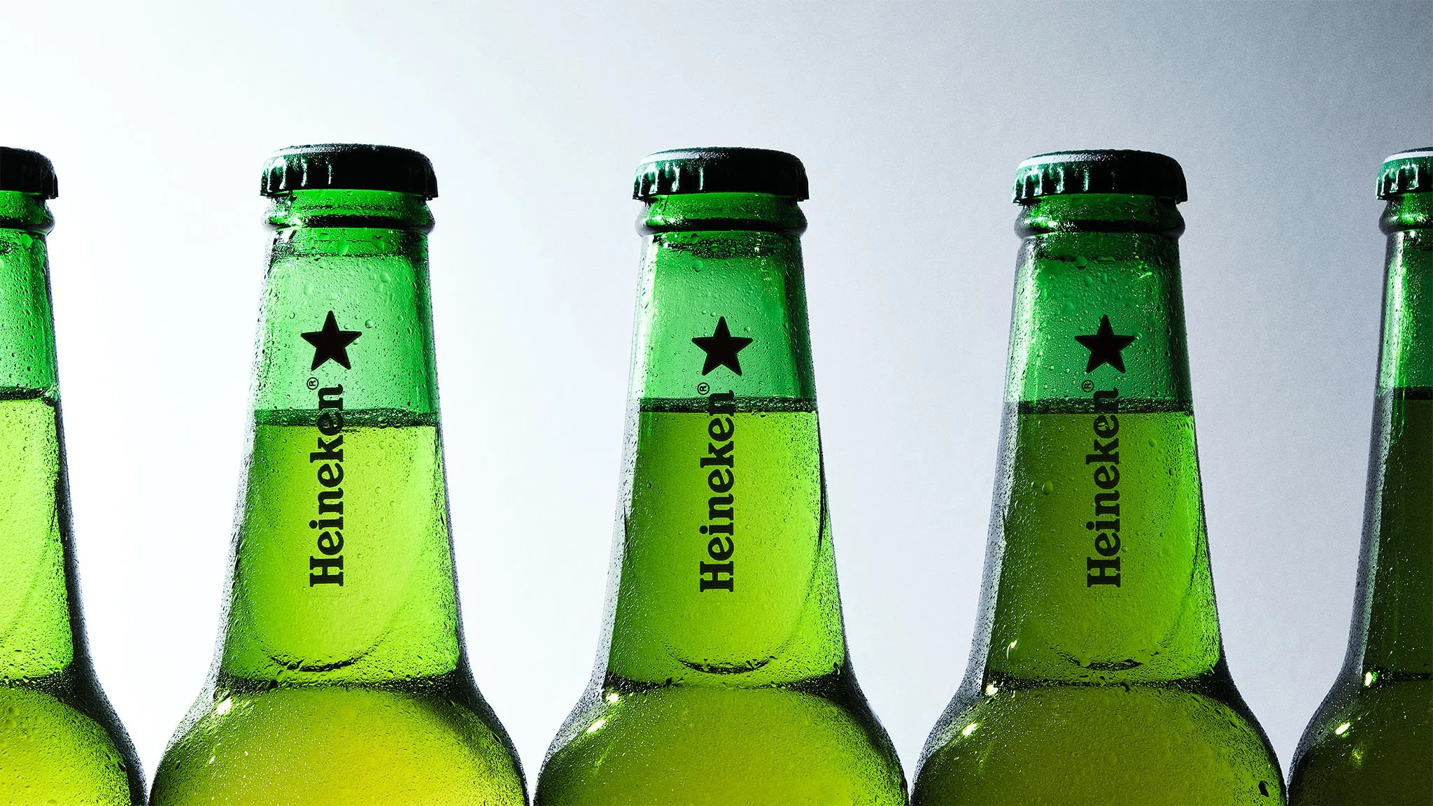 Close-up of several green Heineken beer bottles with condensation, positioned against a plain background.