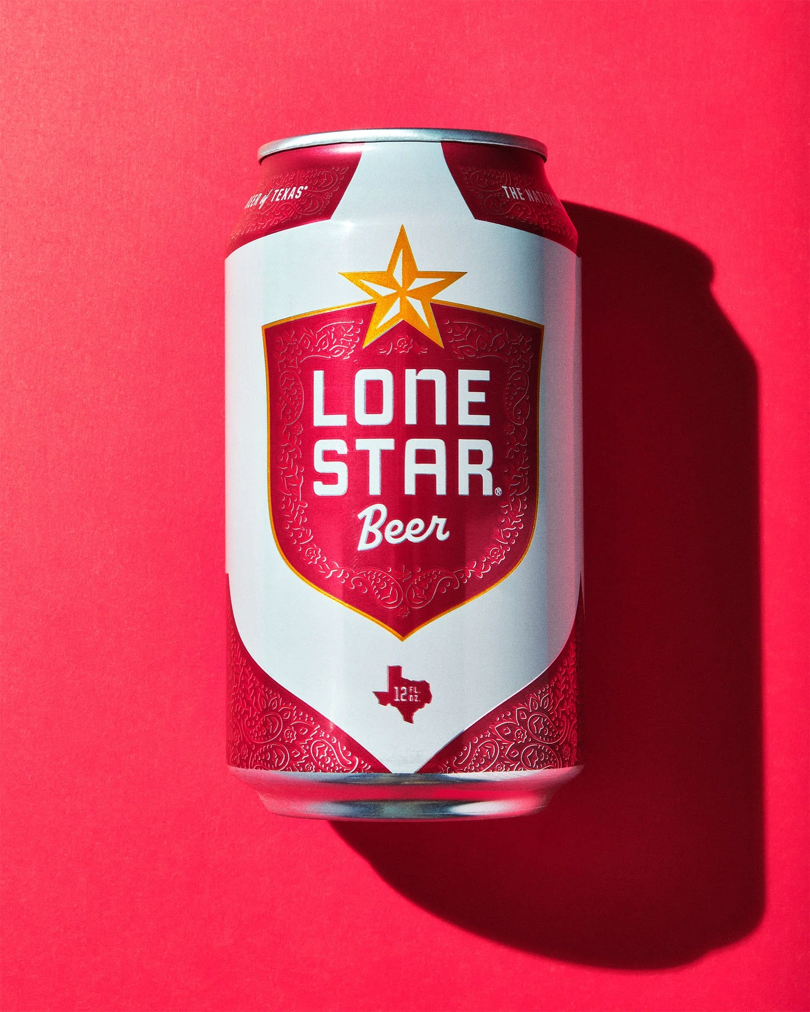A can of Lone Star Beer with a red and white label, a gold star, and a Texas shape icon, placed on a red background.