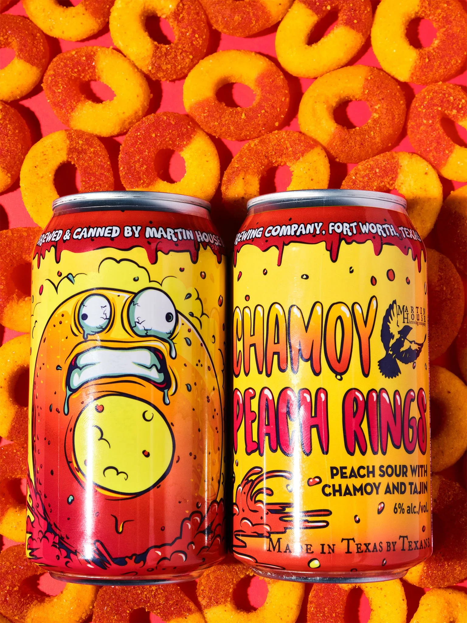 Two cans of Chamoy Peach Rings, peach sour beverage with Chamoy and Tajín flavor, surrounded by peach rings snack candies on a pink background.