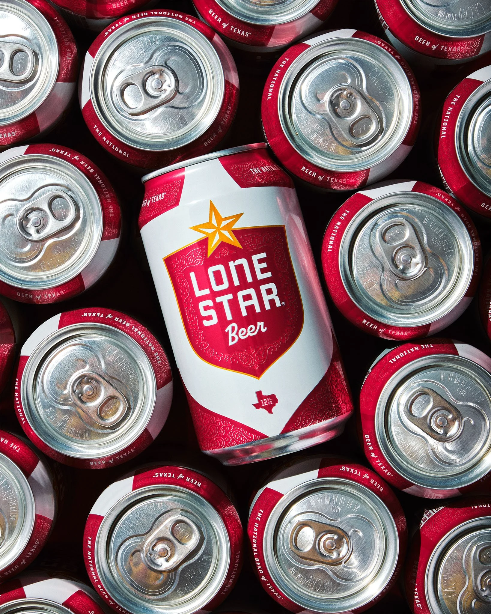 A can of Lone Star Beer surrounded by multiple other cans of Lone Star Beer. The cans are silver with red and white labels, and the one in the center features a large red and white design with a yellow star and the text "Lone Star Beer," along with a small Texas state outline.