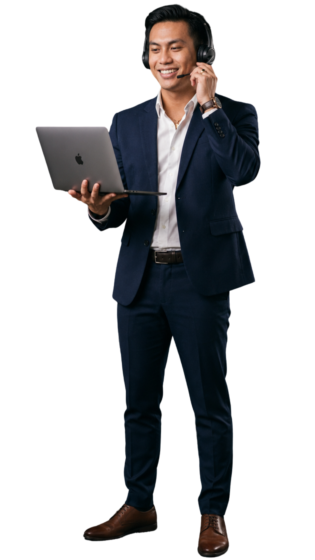 A man in a navy blue suit and brown dress shoes holding a silver MacBook laptop, wearing headphones, and smiling.