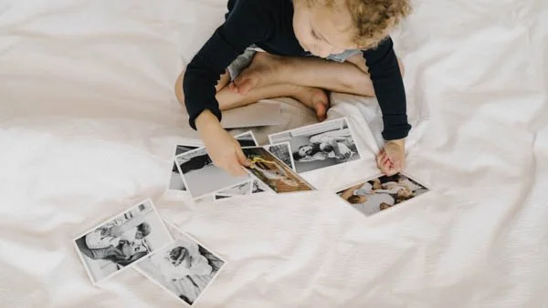 Child on a bed looking through printed family photographs and keepsake photo prints, showcasing quality prints of everyday moments by Framed.
