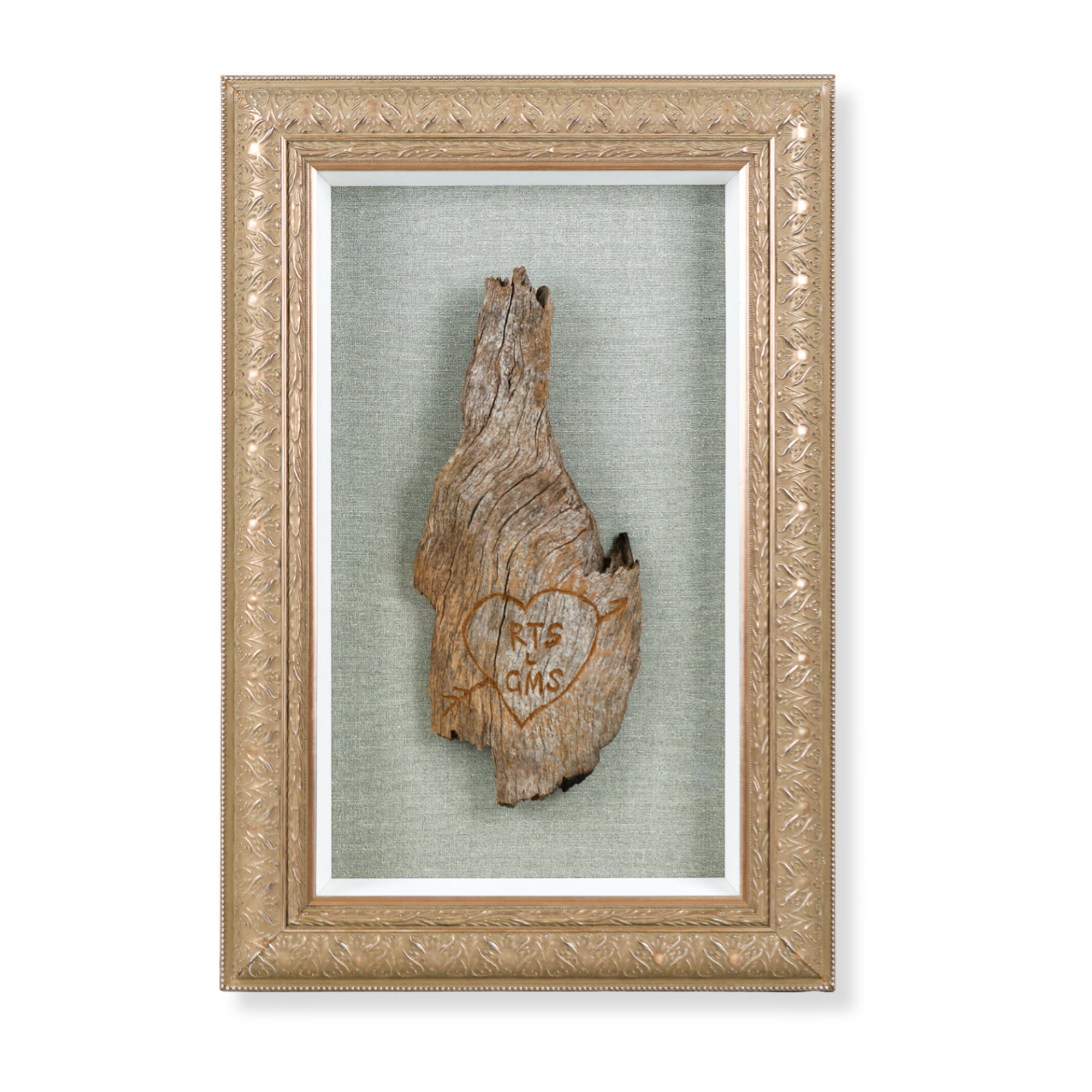 Custom framed carved tree bark keepsake featuring engraved initials and a heart motif, with a textured linen mat, white timber inner frame and ornate gold frame. 