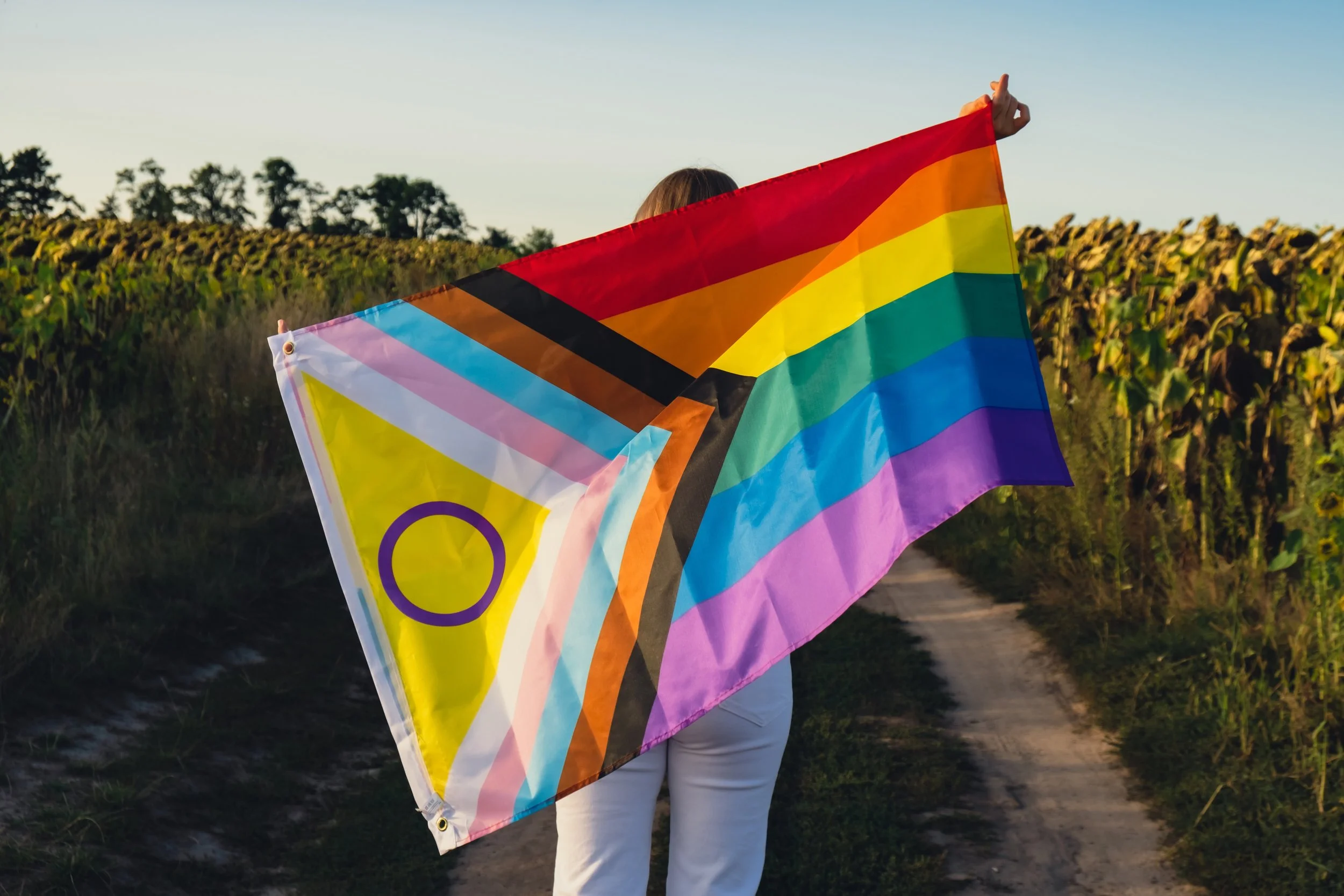 Woman holding a Pride flag in a field.