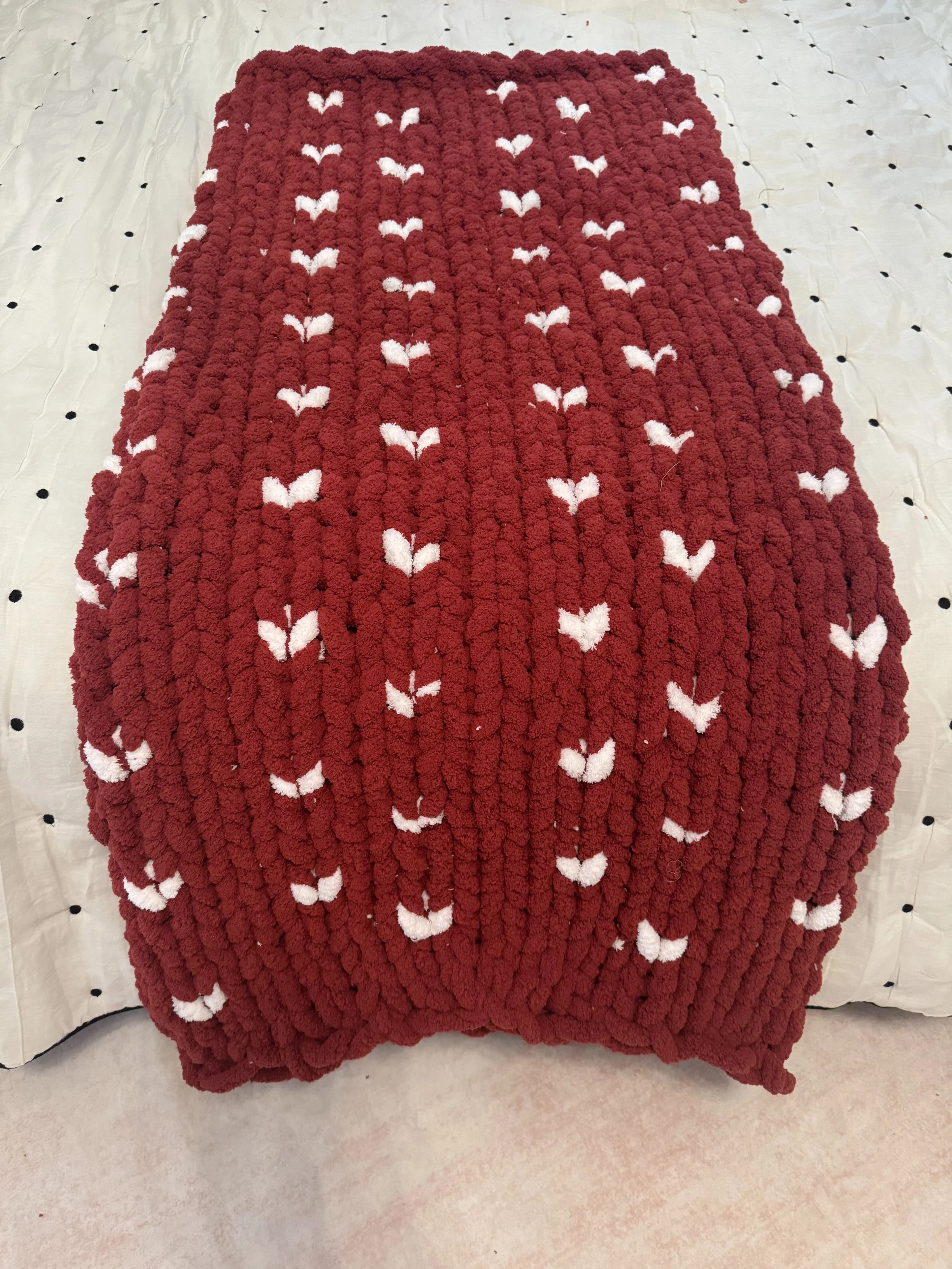 Red knitted blanket with white hearts pattern on a bed.