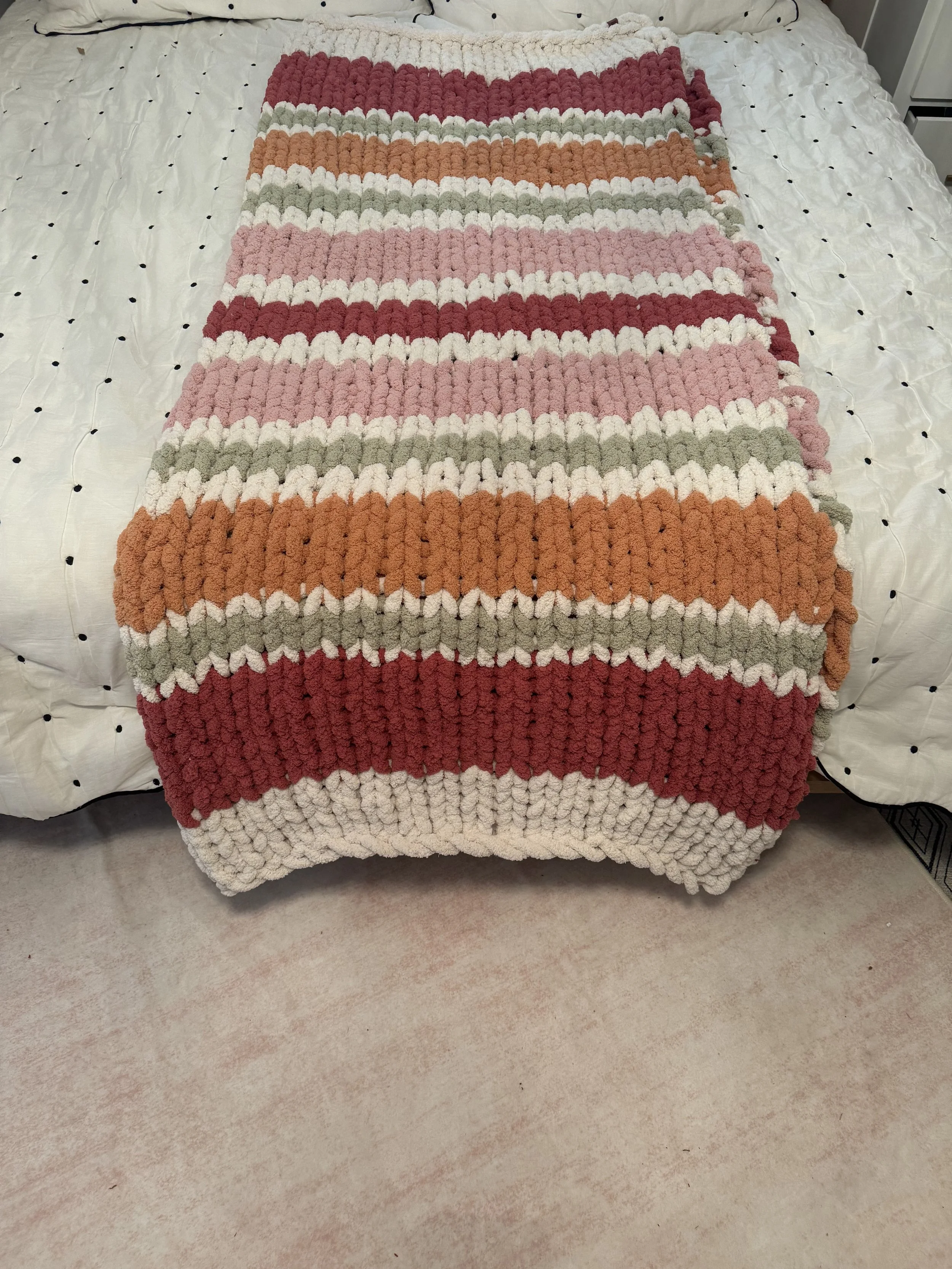 Colorful chunky striped knit blanket on bed.
