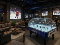 Indoor sports bar with multiple TV screens showing hockey games, a hockey-themed ice skating table game, and seating areas.