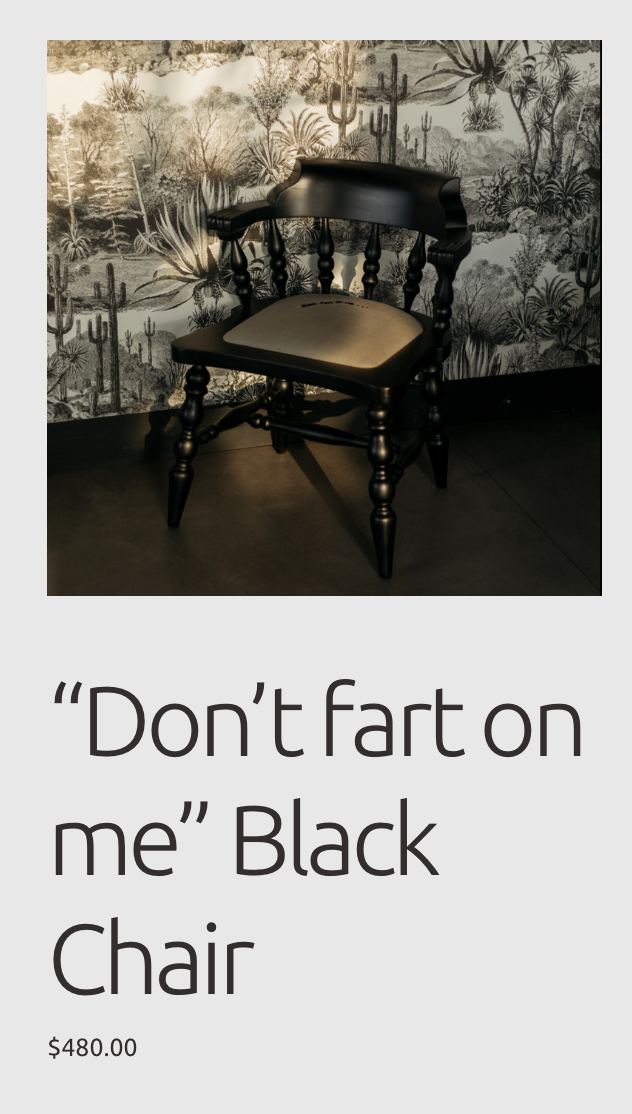 Black wooden chair with a cushioned beige seat and a decorative backrest, positioned against a background with a cactus and desert plants wallpaper.
